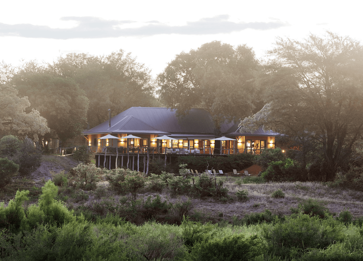 Lodge illuminated at sunset amidst lush greenery.