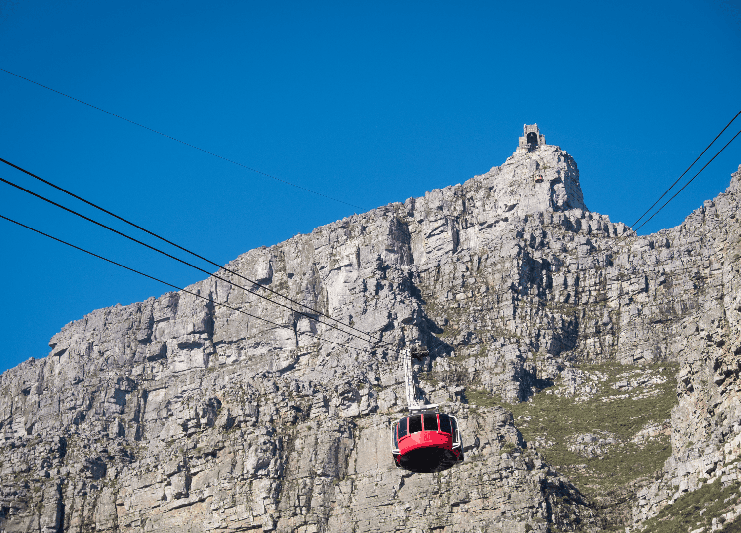 Red cable car ascending rocky mountain peak.