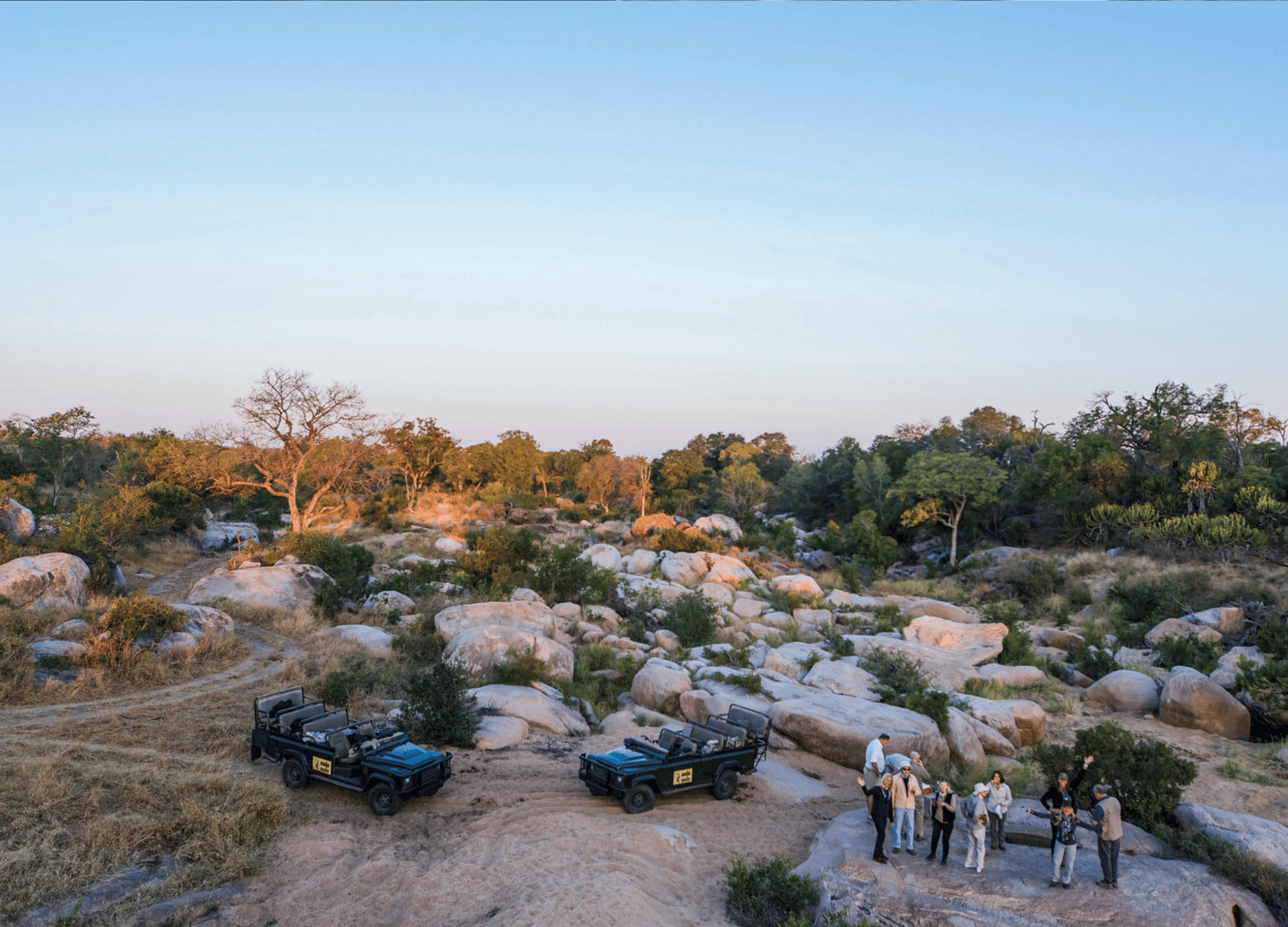 Safari vehicles and people in rocky landscape.