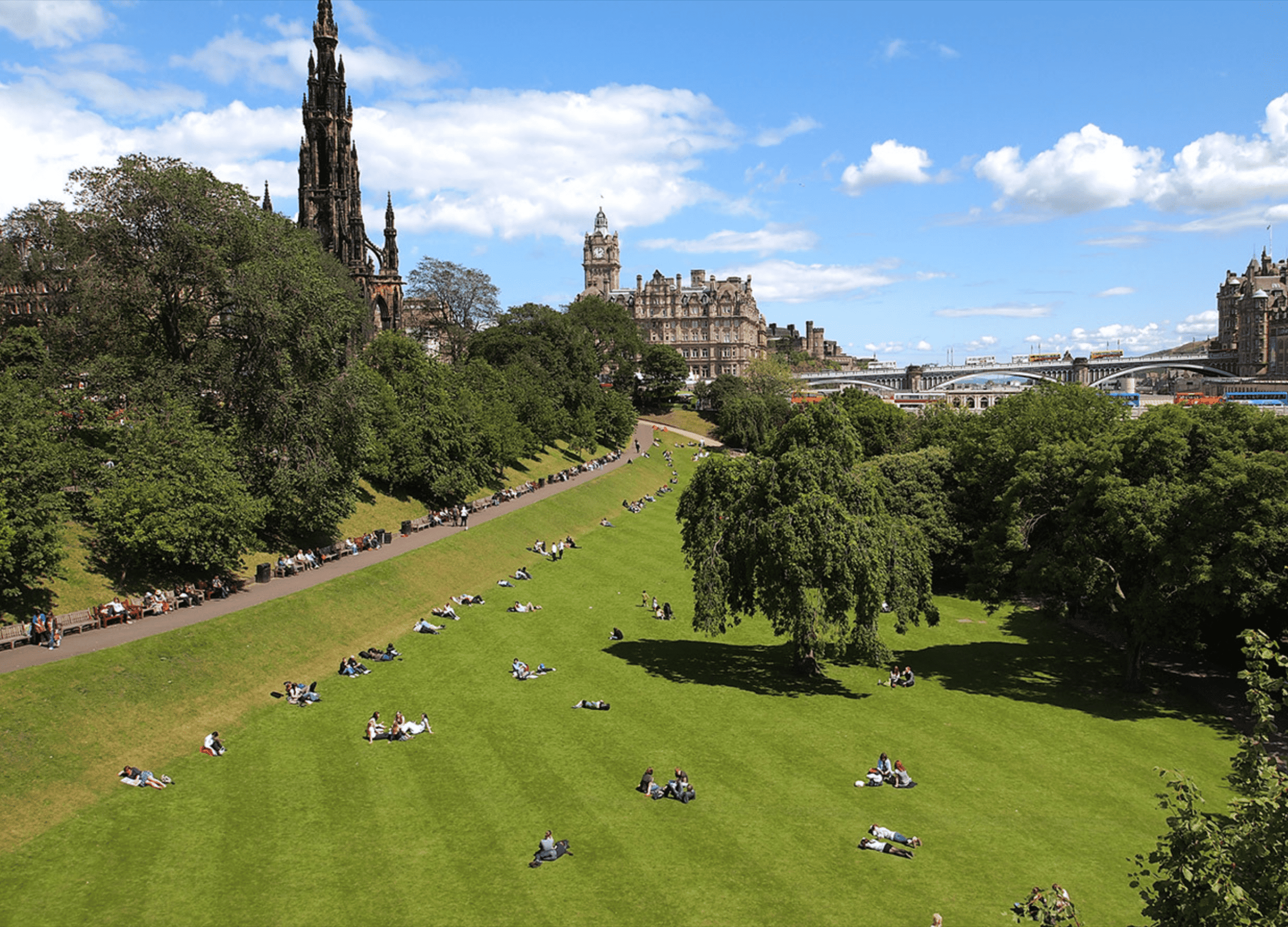 People relaxing in lush Edinburgh park under blue sky.