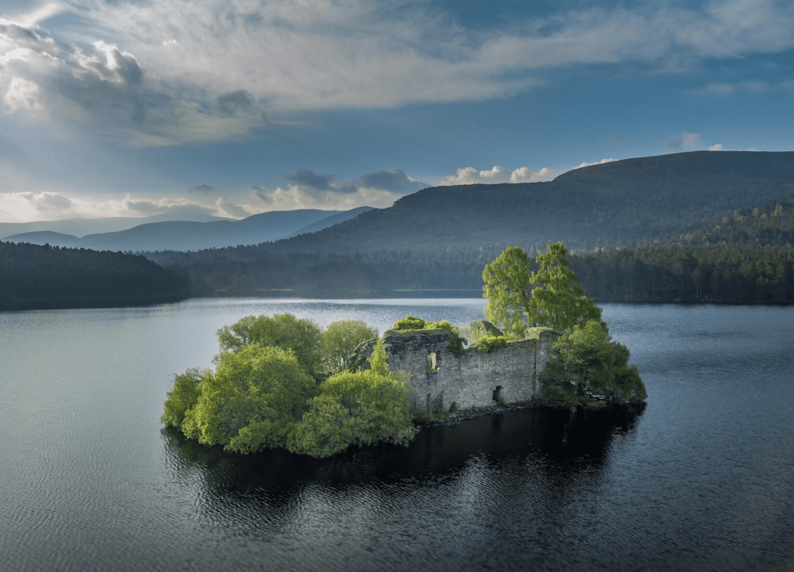 Island ruins on tranquil lake, mountainous background.