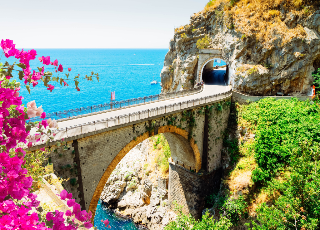 Scenic coastal bridge with vibrant flowers and sea view.