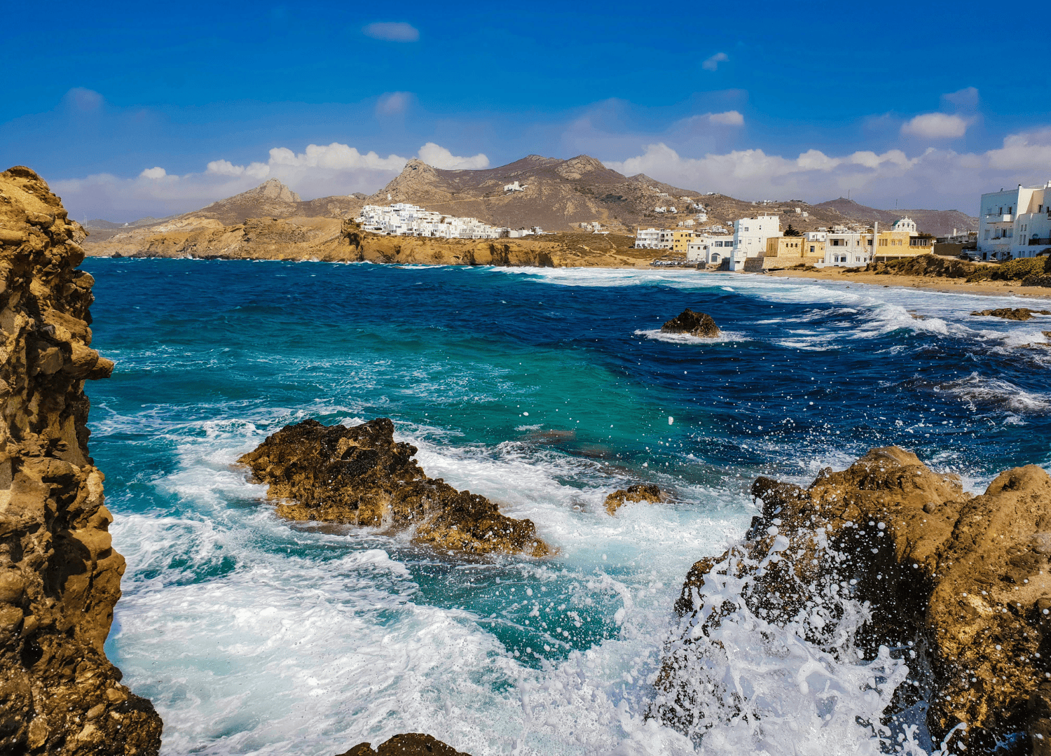 Rocky coast with waves and distant buildings.