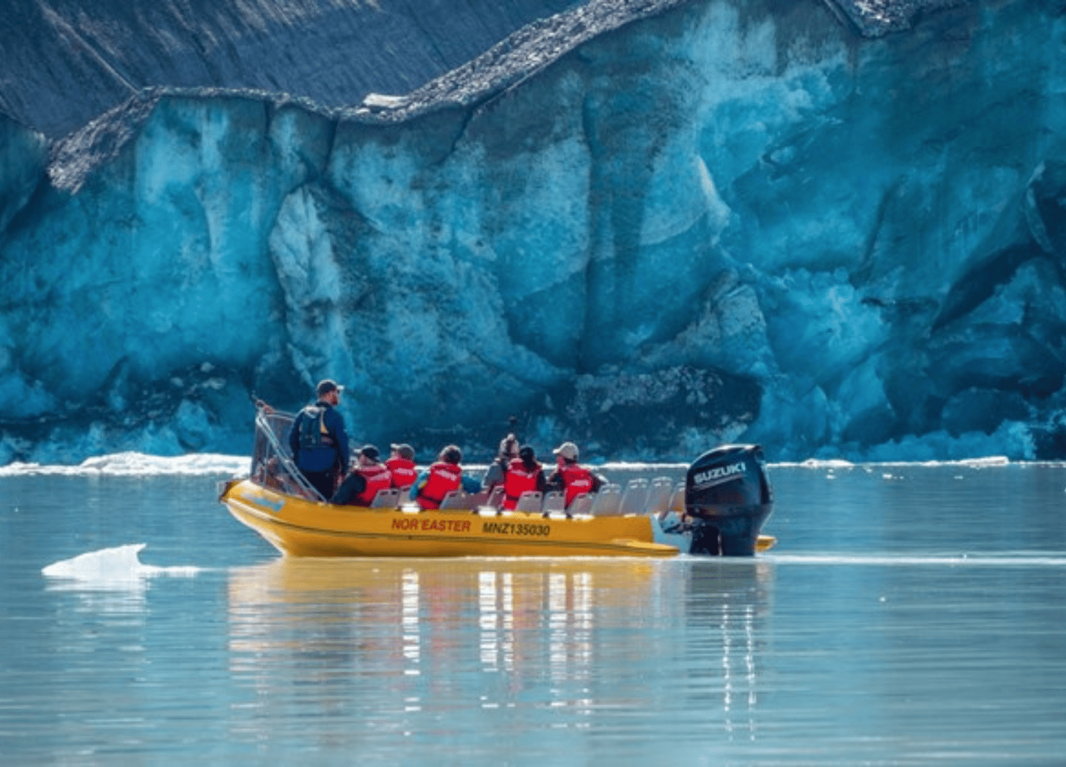 Yellow boat with passengers near a blue glacier.