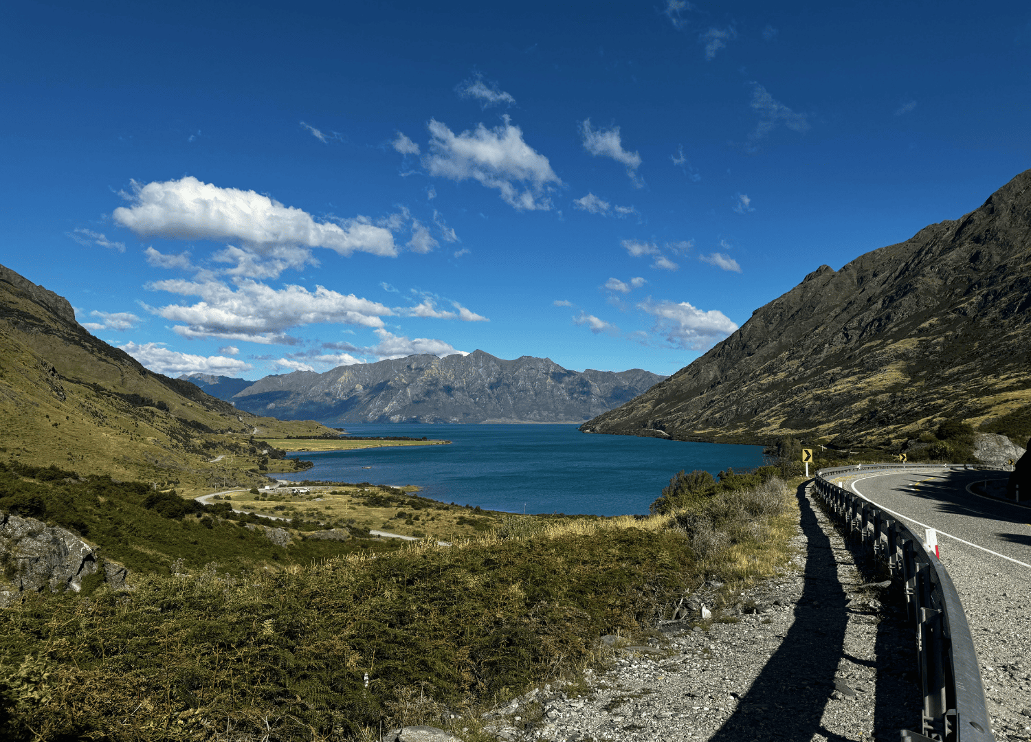 Mountain road by lake under blue sky