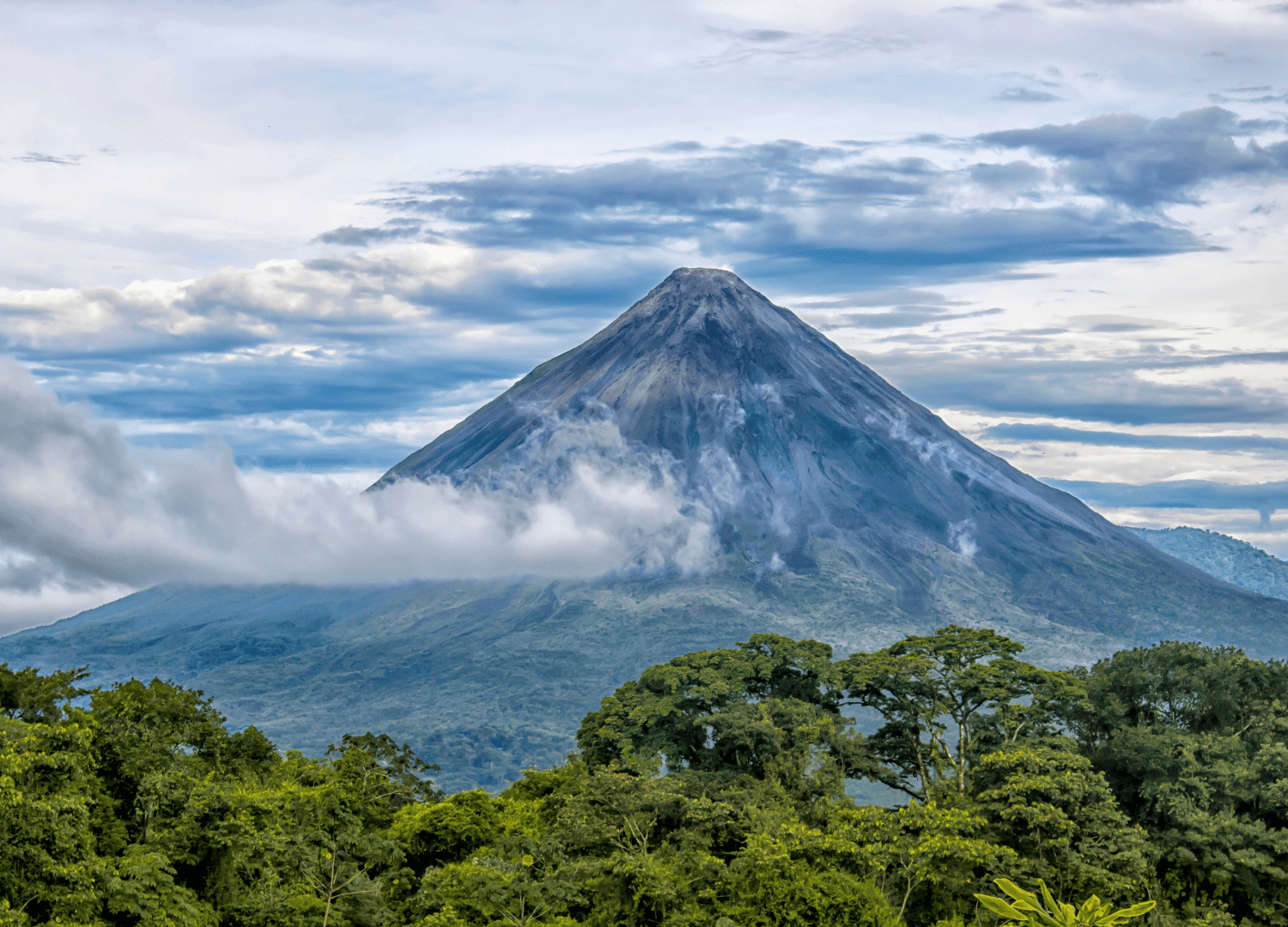 Majestic volcano with clouds and lush forest.