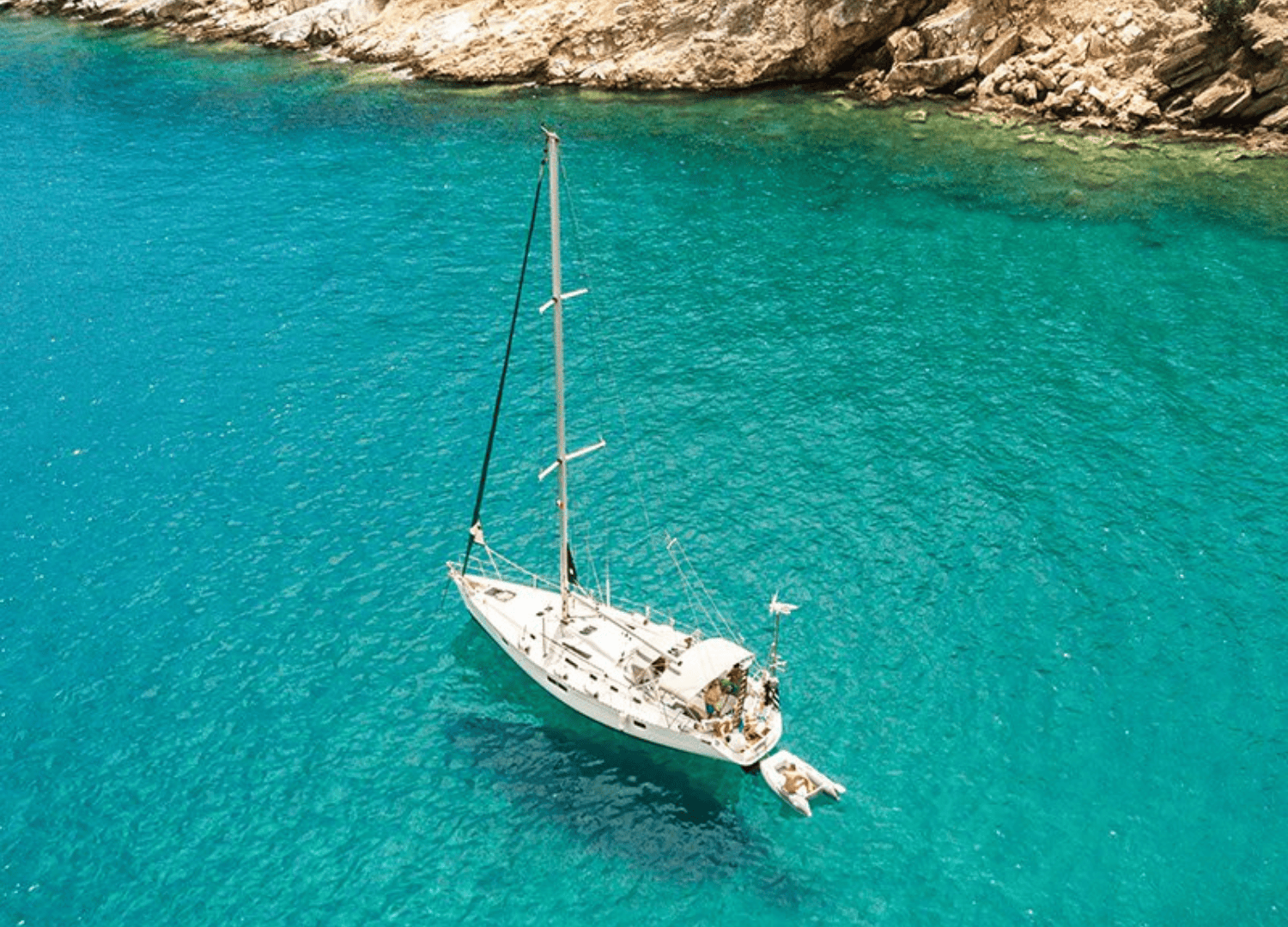 Sailboat on clear turquoise sea near rocky coast.