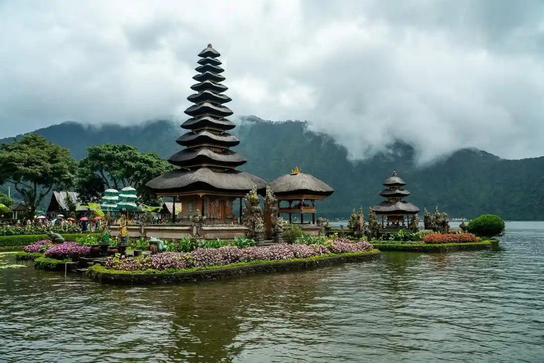 Balinese temple on lake with mountains and clouds.